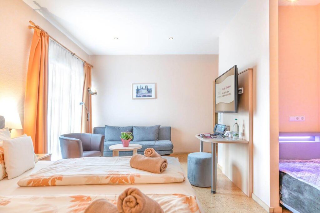 Komfort-Zimmer mit Doppelbett, Sessel, Sofa, Flat-TV, Schreibtisch und Einzelbett.