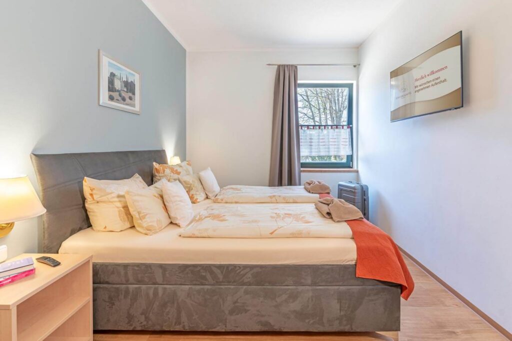 Schlafzimmer mit großem Doppelbett, Nachttischen und TV an der Wand sowie einem Fenster.